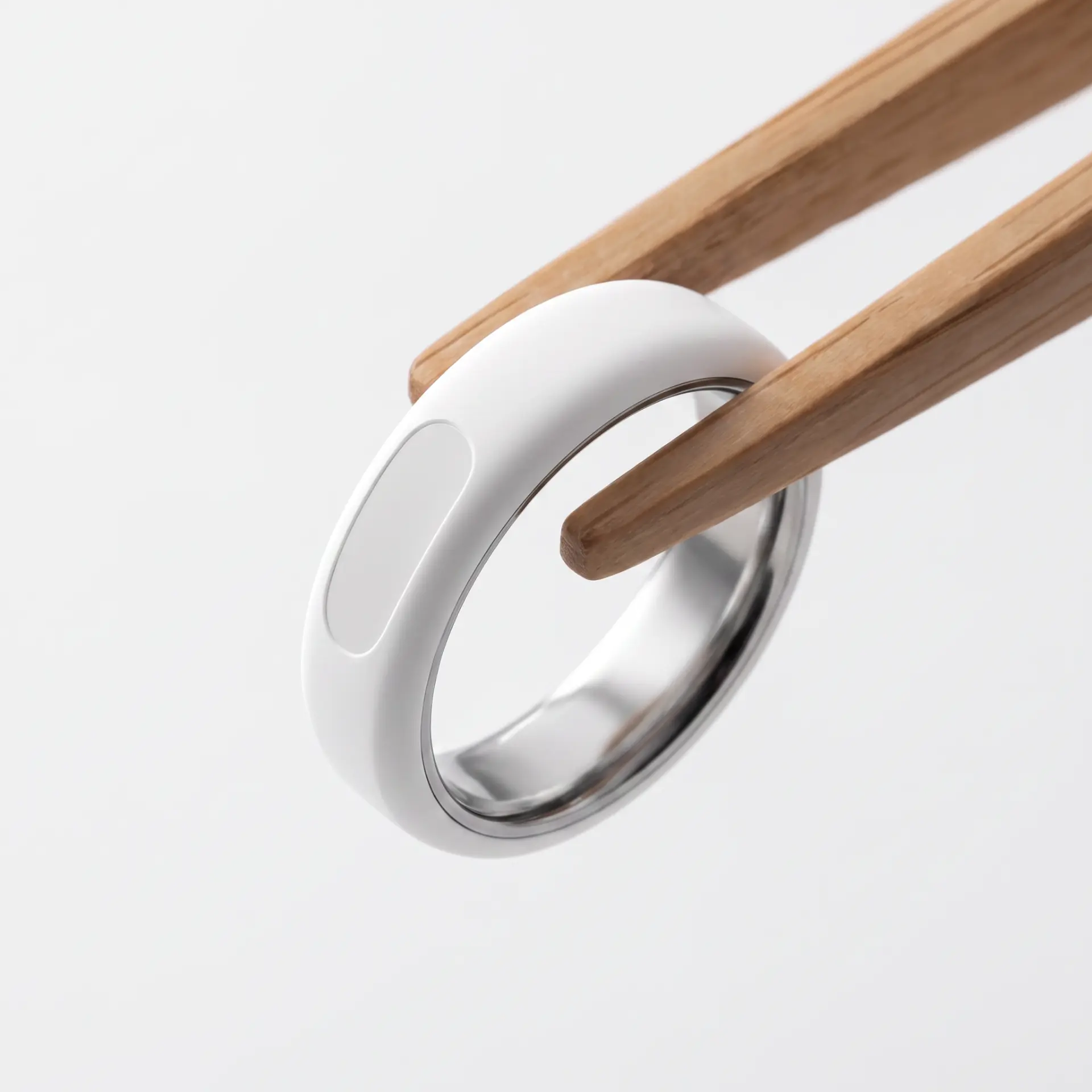 R1, a white ceramic ring with a polished steel interior, held by wooden tongs